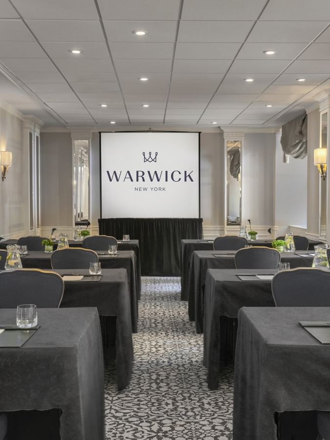 Essex room with black-covered tables, gray chairs, and water pitchers facing a screen at Warwick New York