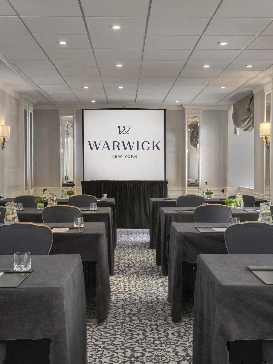 Essex Classroom table set-up facing large screen with glasses & green floral arrangements at Warwick New York