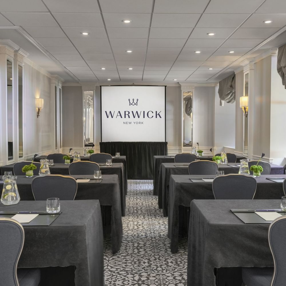 Essex Classroom table set-up facing large screen with glasses & green floral arrangements at Warwick New York