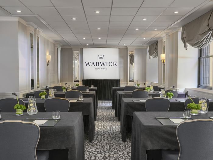Essex Classroom table set-up facing large screen with glasses & green floral arrangements at Warwick New York