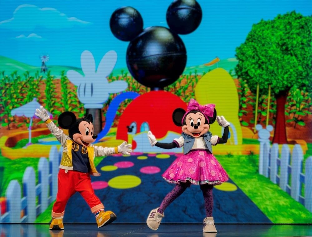 Mickey and Minnie in contemporary costumes dance onstage in front of a projection in a show that's appropriate for toddlers at Walt Disney World. 