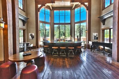 Warm lodge space by a tall windows and a curved bar a piano at Hotel Park City Autograph Collection 