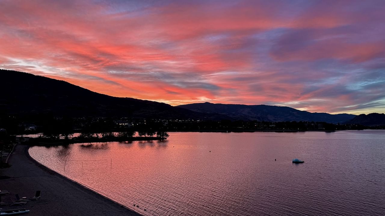 Sunset view over a calm lake, with pink and orange hues and silhouetted mountains in the background.