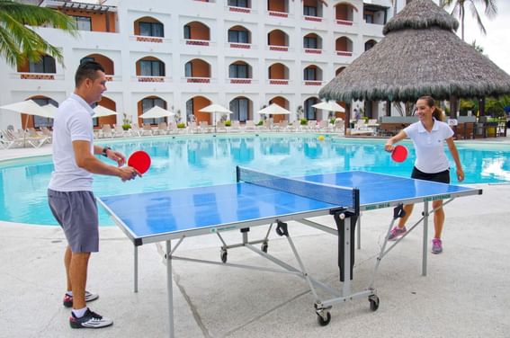 A man and woman playing table tennis by the pool at Plaza Pelicanos Club Beach Resort