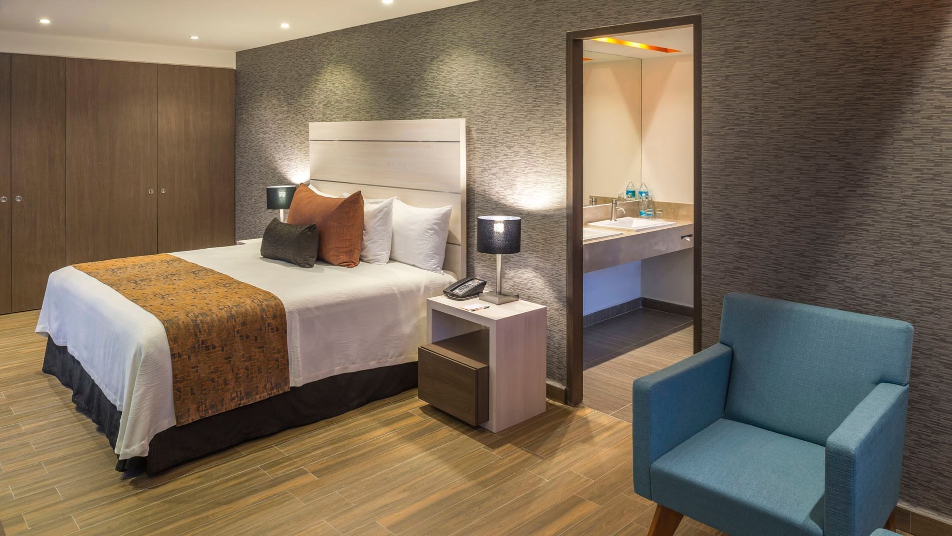 King Presidential Suite at Real Inn Celaya showing the plush king bed and an open doorway into the modern bathroom