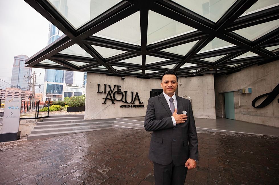 A person in a suit standing in front of the Live Aqua Hotels & Resorts Residence entrance