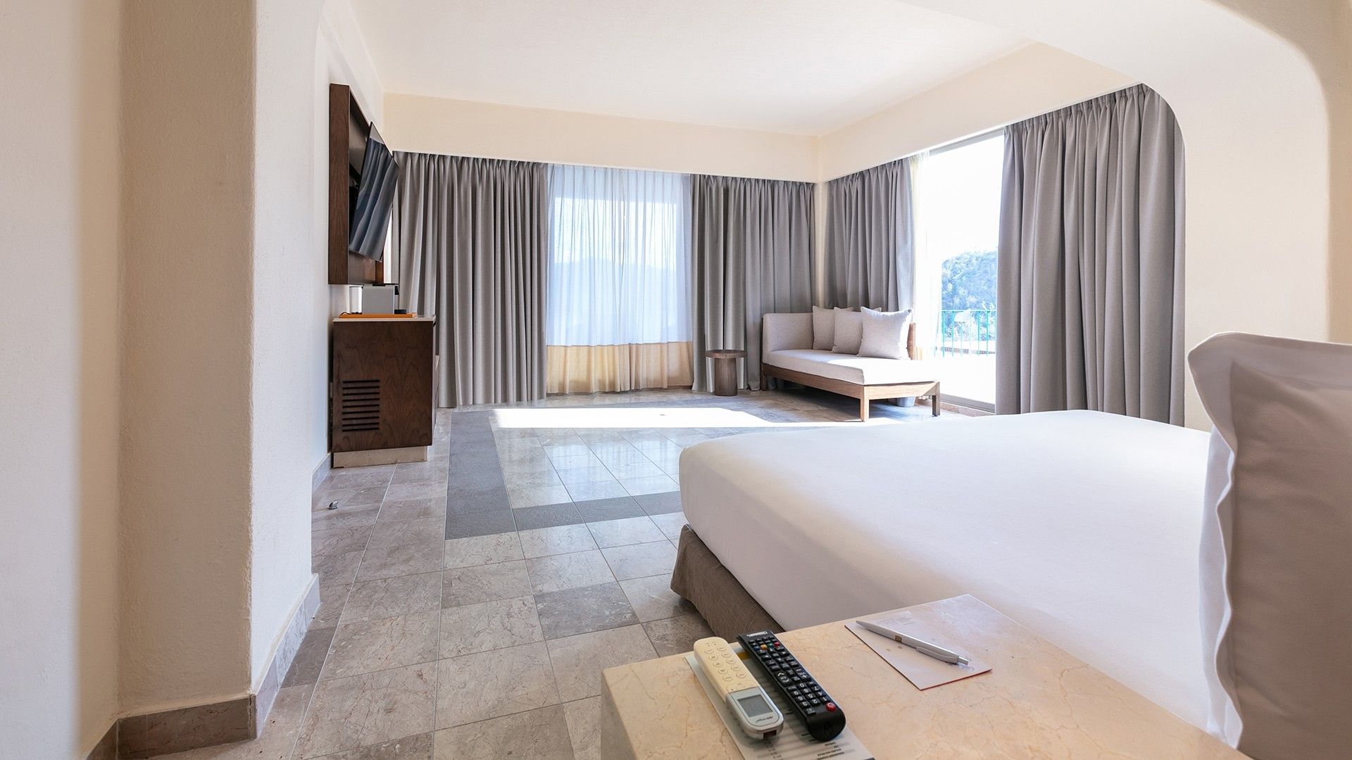 King Master Suite bedroom with tiled floors, grey curtains, and a daybed by a large window at Camino Real Acapulco Diamante