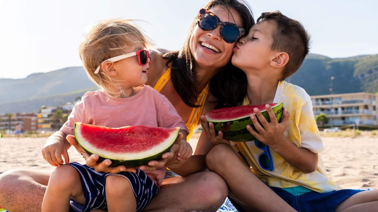 mom sharing watermelon with kids on the beach