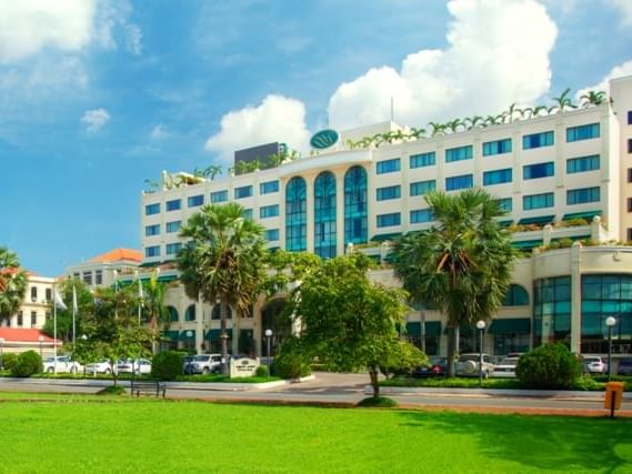 The grand facade of Sunway Hotel Phnom Penh on a sunny day, with palm trees and a manicured green lawn