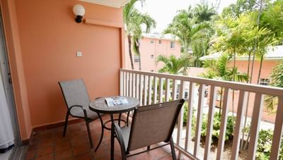 Standard Room balcony with two mesh chairs and a small round table overlooking palm trees outside Worthing Court Apartment