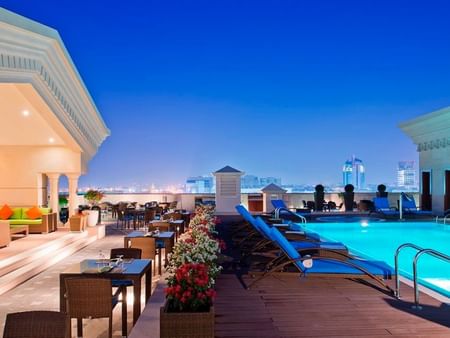 Rooftop pool with lounge chairs in Moon Deck at night in Warwick Doha