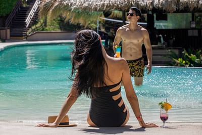 A lady sitting on the edge of a pool with a drink at Villas Sol Beach Resort