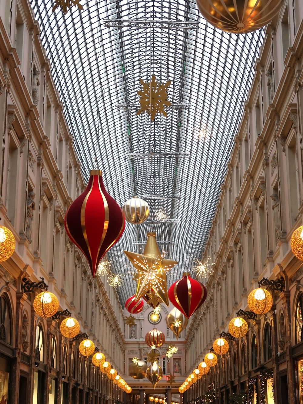 Overdekte winkelgalerij met feestelijke kerstversiering, grote rode en gouden kerstballen en verlichte sterren