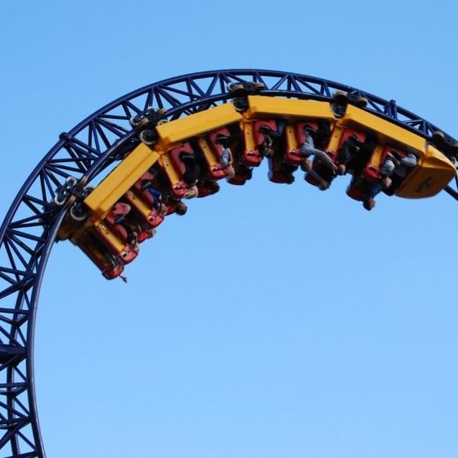 A yellow and red rollercoaster car suspended upside down on a curved black track against a clear blue sky at Thorpe Park