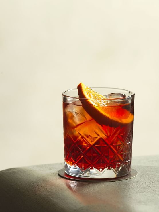 Cocktail at Elysium Manly featuring a glass with an orange slice by a ledge under warm light in Cibaria\'s 55 North Bar