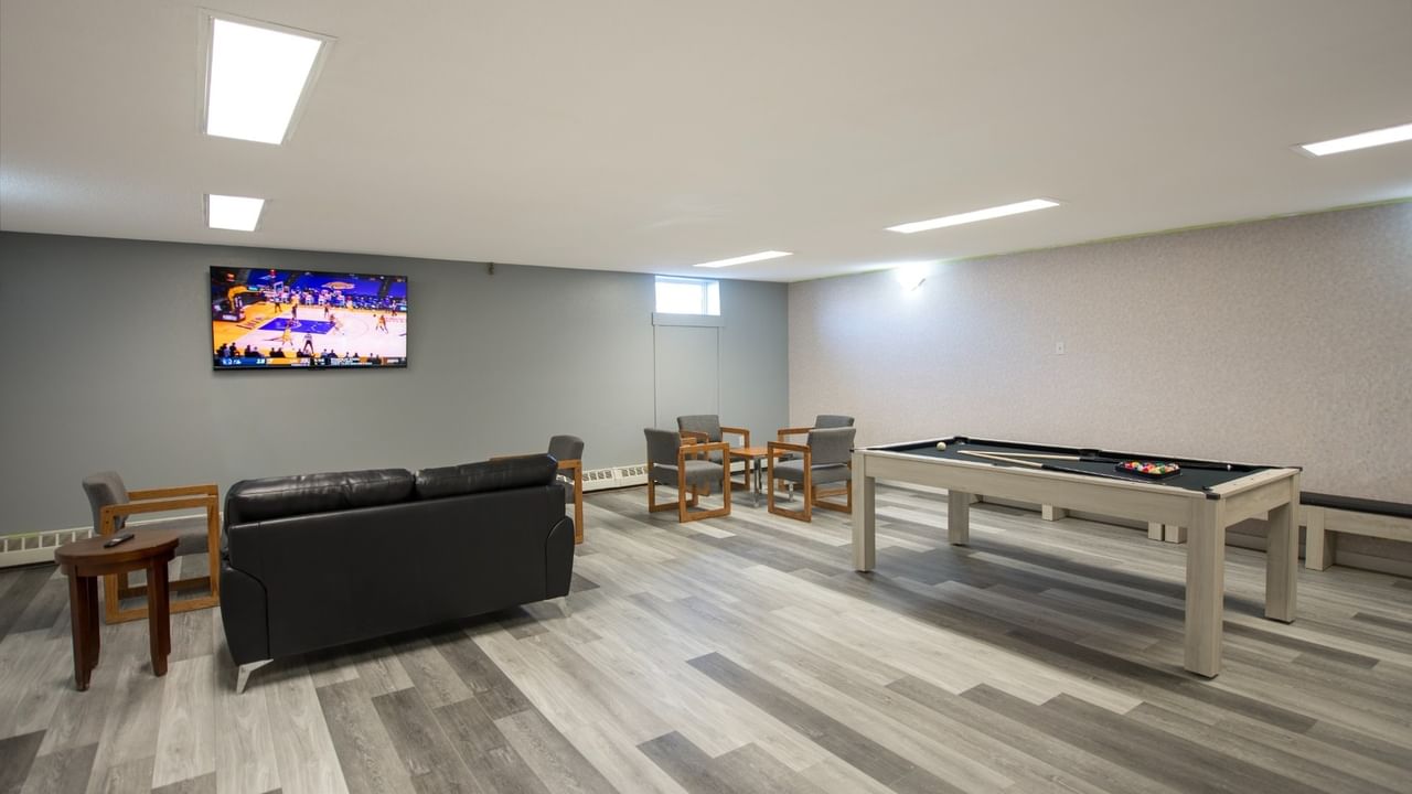 Game room with pool table, black couch, chairs, and TV showing basketball game.