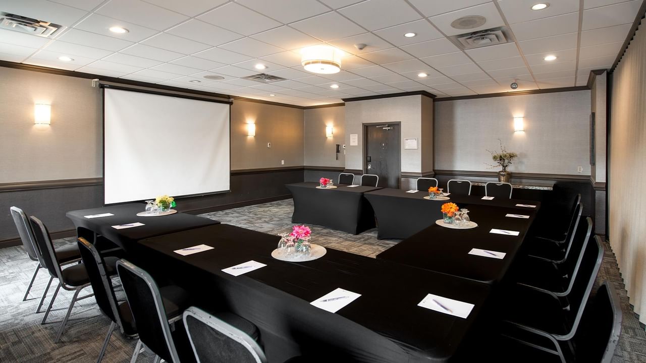 Meeting room with U-shaped table setup, projection screen, and colorful floral centerpieces at Coast Calgary University Area Hotel by APA