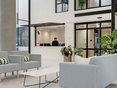 Modern lobby with light gray seating, potted plants, and reception desk at UniLodge Auckland Central
