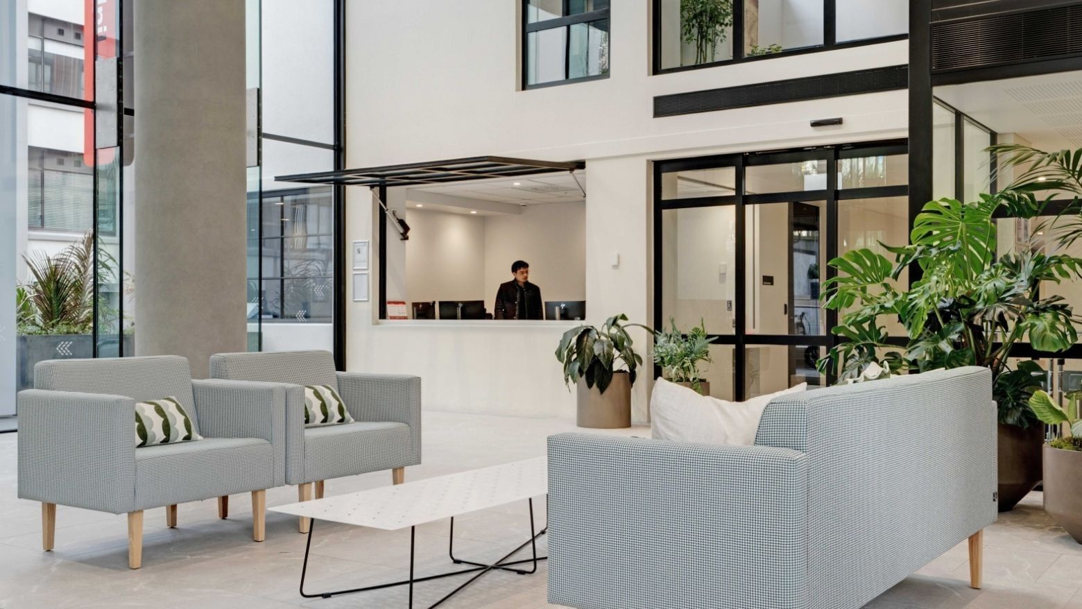 Modern lobby with light gray seating, potted plants, and reception desk at UniLodge Auckland Central