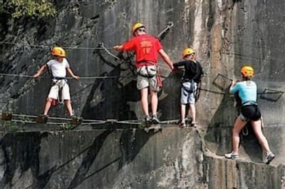 Family climbing a rocky cliff using safety harnesses & helmets on a challenging outdoor route near Blackstone Mountain Lodge