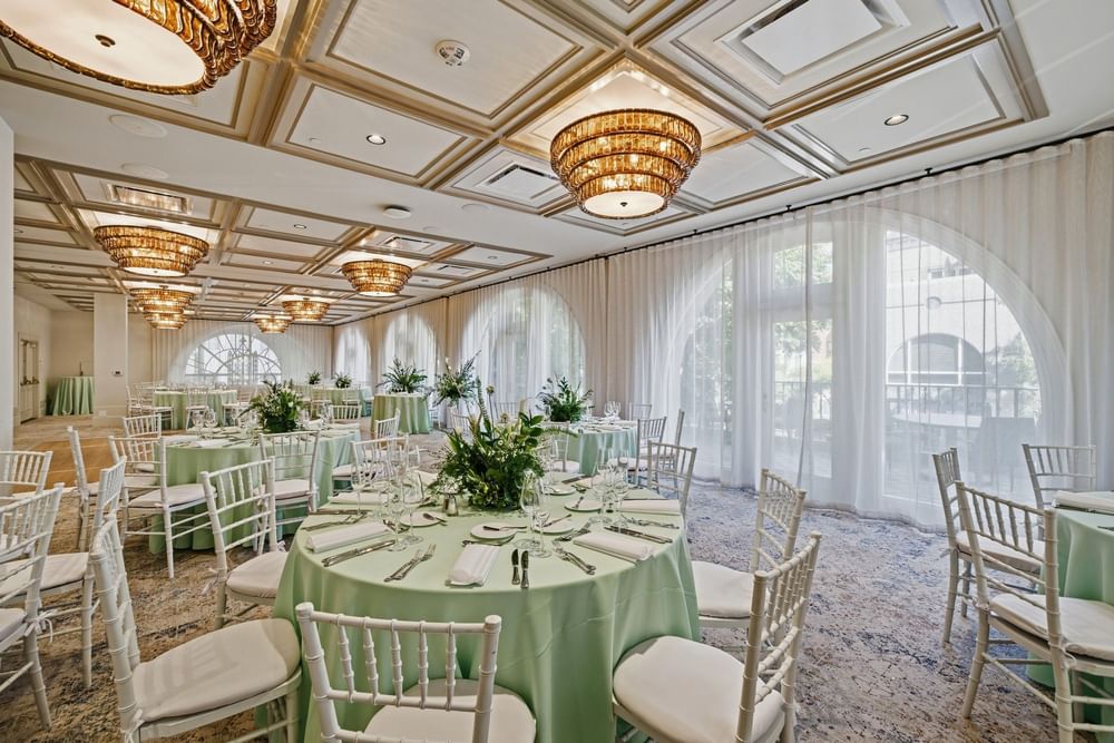 Elegantly set banquet hall with round tables, white chairs, and green tablecloths at El Prado Palo Alto