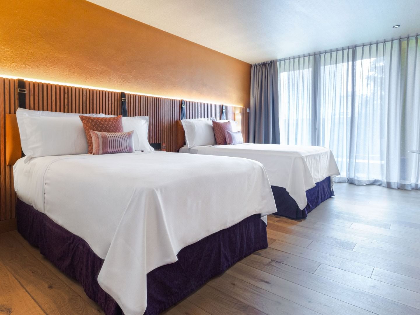 2 Double Superior Camino Real Club with purple bed skirts and light wood flooring by a window at Camino Real Polanco Mexico