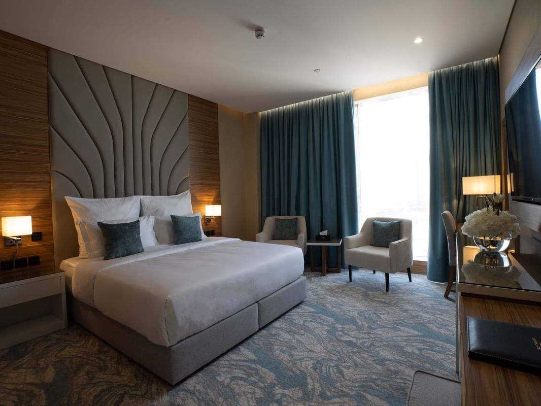 King bed with grey pillows by armchairs under blue curtains in Executive Suite at Cantonal Hotel by Warwick Riyadh