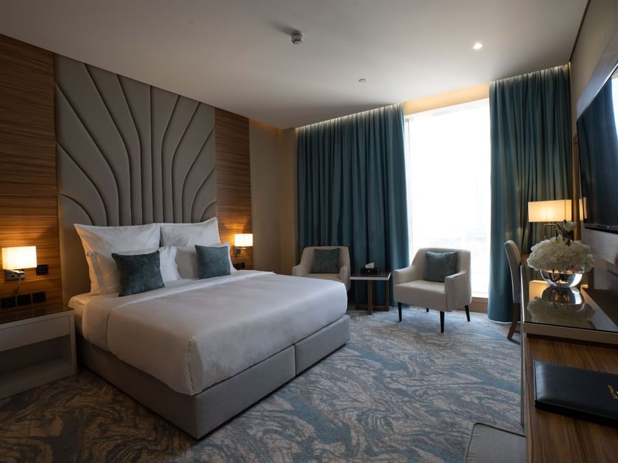 King bed with grey pillows by armchairs under blue curtains in Executive Suite at Cantonal Hotel by Warwick Riyadh