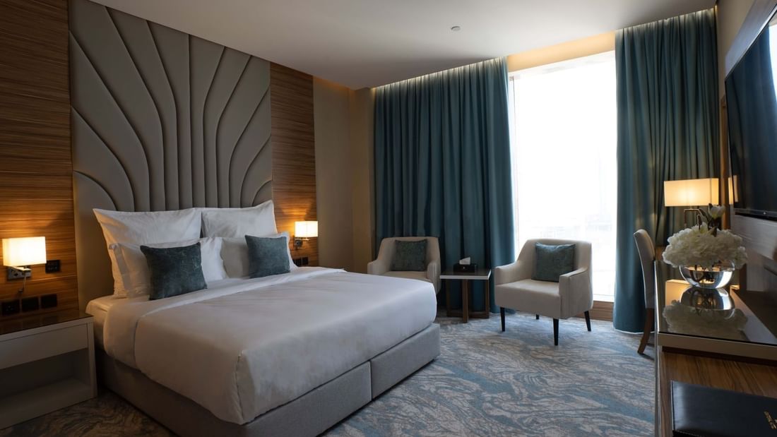 King bed with grey pillows by armchairs under blue curtains in Executive Suite at Cantonal Hotel by Warwick Riyadh