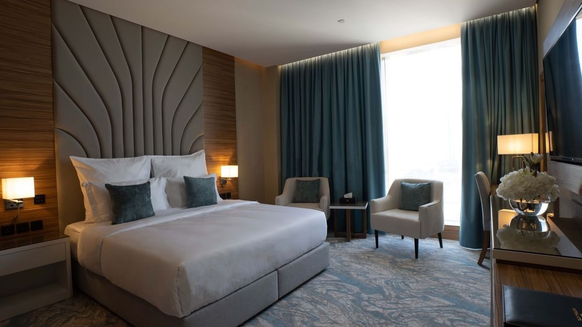King bed with grey pillows by armchairs under blue curtains in Executive Suite at Cantonal Hotel by Warwick Riyadh