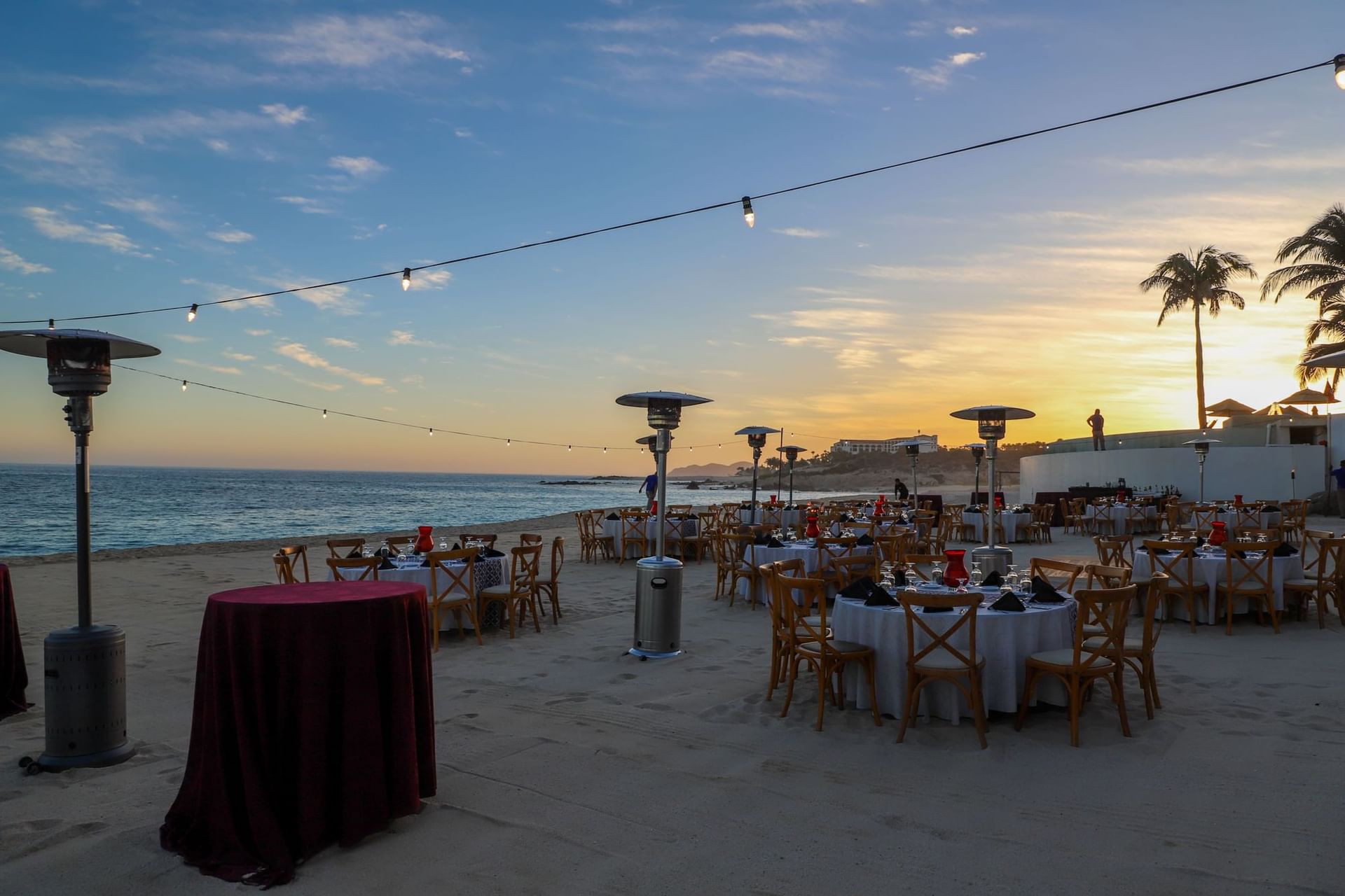 Rooftop dining event with round tables, string lights, and ocean views at sunset in Marquis Los Cabos Resort