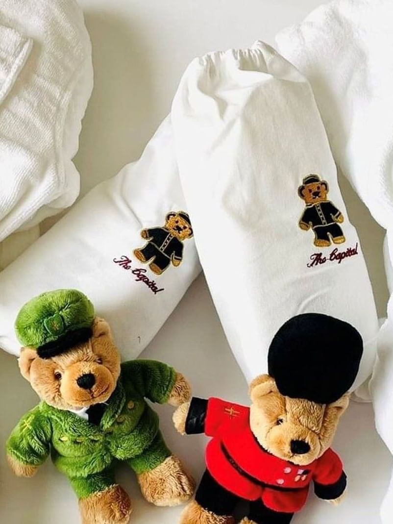 White robes by two plush teddy bears in uniforms on a bed at The Capital Hotel, Apartments and Townhouse