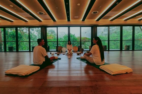 Three people in a yoga session with a forest view through large windows at El Silencio Lodge & Spa