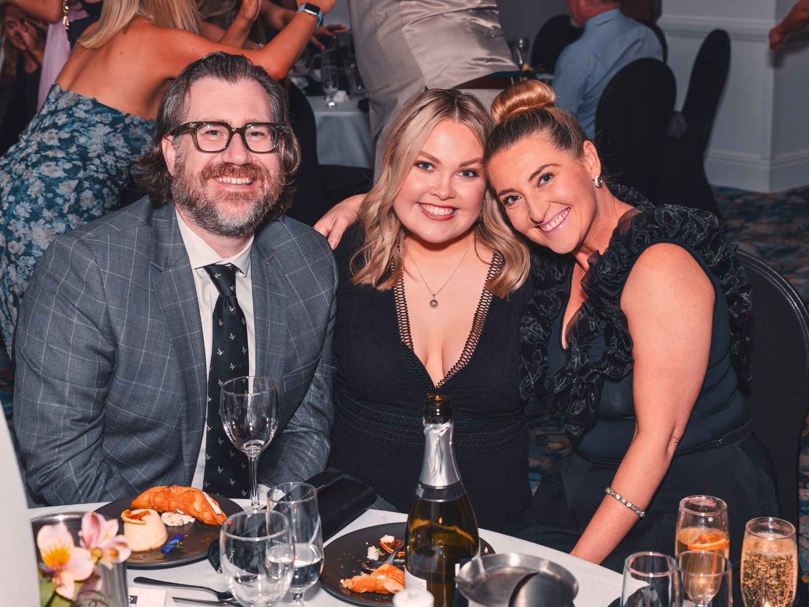 three people sitting at a function banquet event table with dessert
