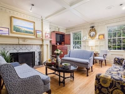 Blue floral sofas by a round coffee table, under a coffered ceiling near a tiled fireplace at Simsbury 1820 House