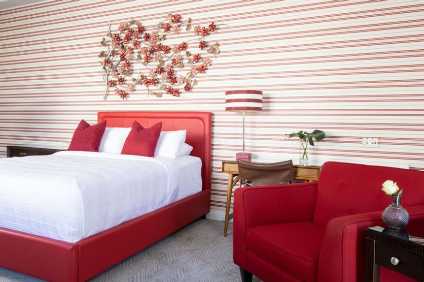 queen bed with red chair beside and red and white striped walls