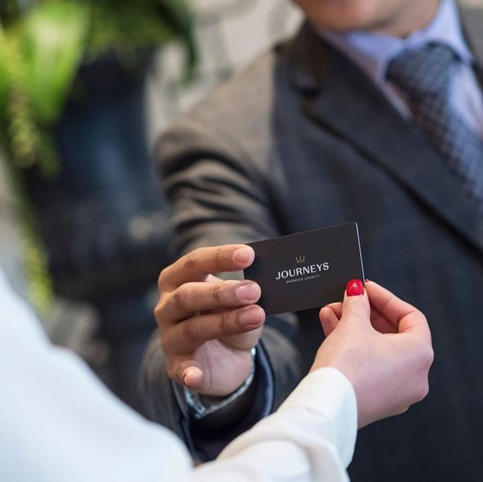 Hand holding a black membership card by a person in a suit in the lobby at Warwick Hotels and Resorts