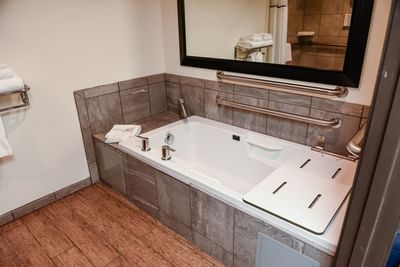 Accessible ​Superior King bathroom featuring a spacious tub with grab bars, a mirror, and tiled walls at Lake Natoma Inn