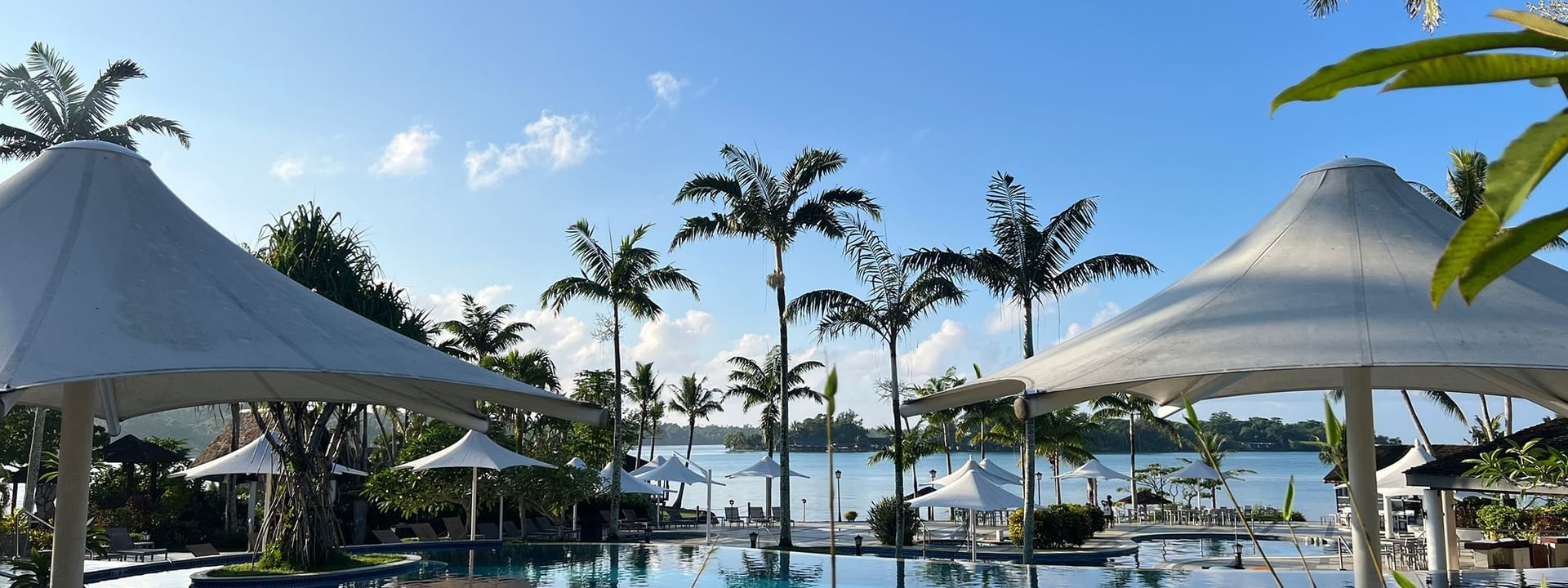 Large pool with beach umbrellas and palm trees at Warwick Le Lagon Efate
