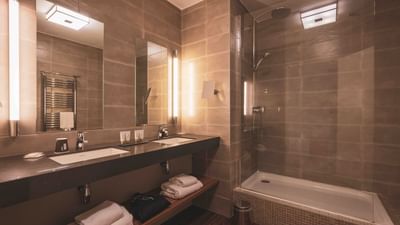 Modern bathroom with two sinks, a glass-enclosed shower, and a wooden shelf with towels.