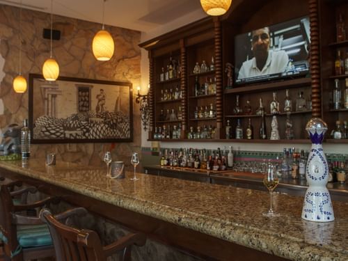 Bar La Suerte with a polished granite counter, stone walls, and a large mural at Hacienda del Mar Los Cabos