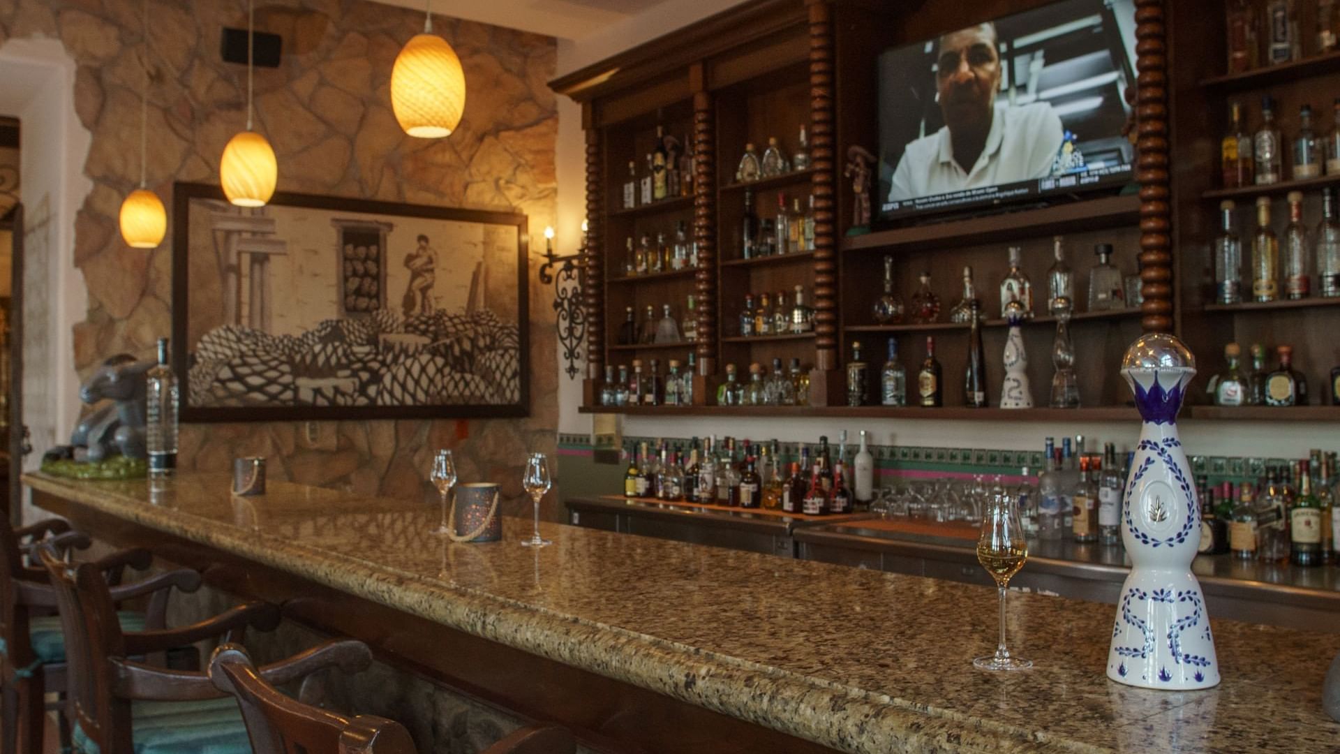 Bar La Suerte with a polished granite counter, stone walls, and a large mural at Hacienda del Mar Los Cabos