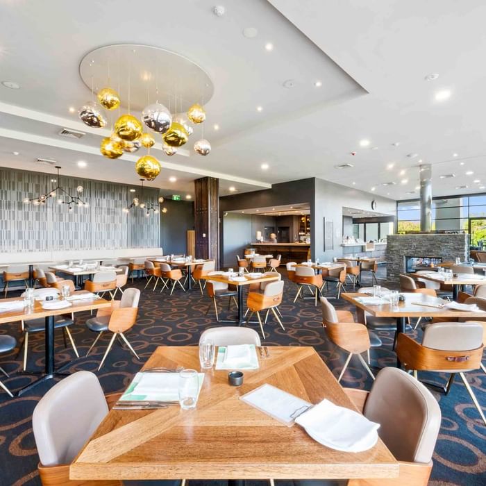 Karinyas Restaurant interior with dining chairs and tables, decorative gold pendant lights at Mercure Kooindah Waters