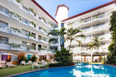 Patio interior con piscina rodeada de palmeras y edificios blancos con balcones en Los Arcos Suites