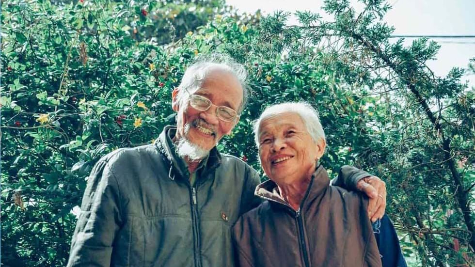 An old couple in jackets standing in front of green shrubbery near Sunway Hotel Georgetown