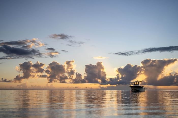 Motorboat by a reflective sea under puffy sunset clouds near Warwick Fiji Resort and Spa