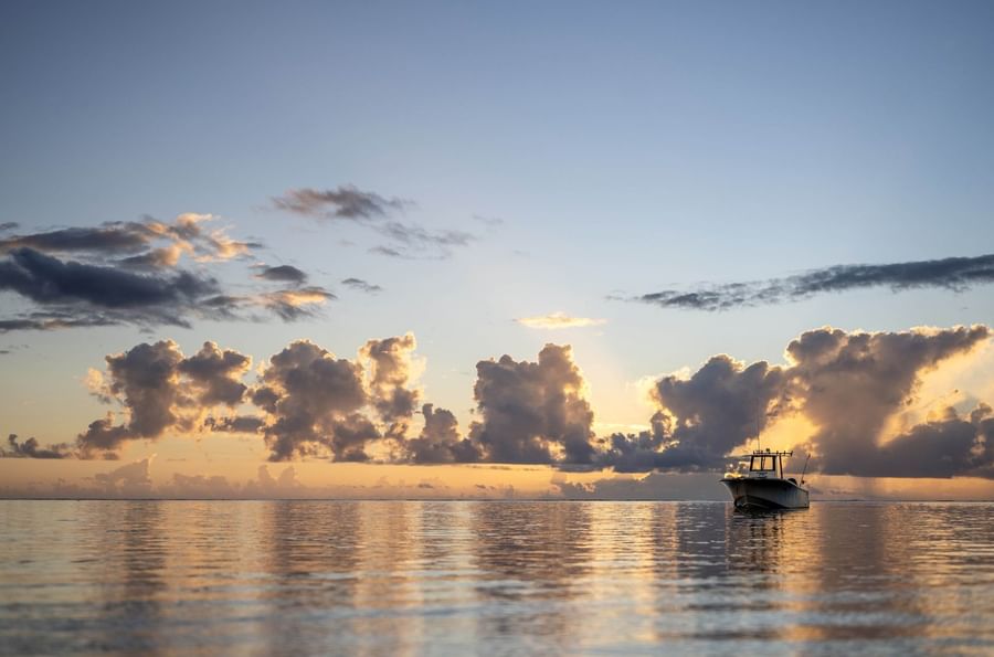 Motorboat by a reflective sea under puffy sunset clouds near Warwick Fiji Resort and Spa