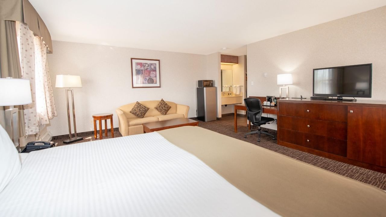 A hotel room with a bed, couch, TV, desk, and refrigerator.