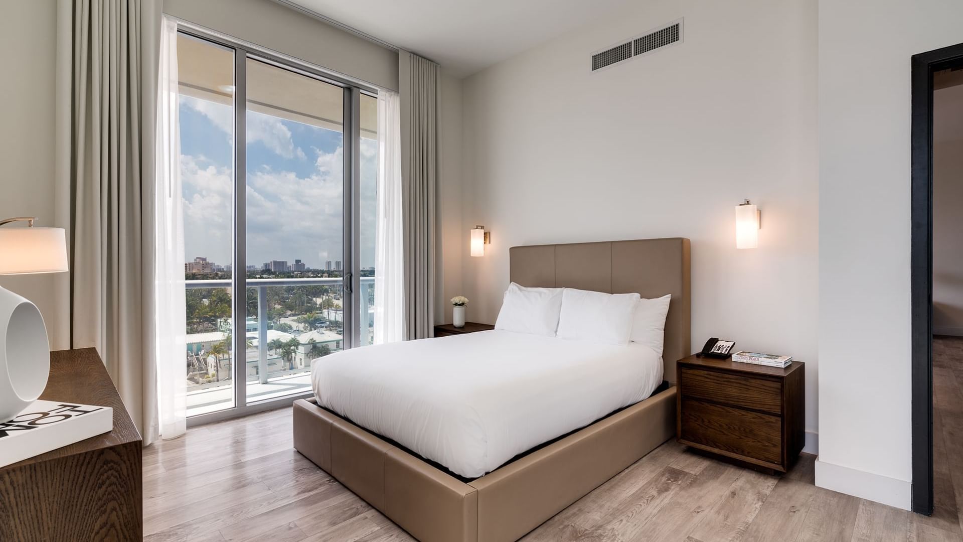 A hotel room with a large bed, two nightstands, and a window with a city view.