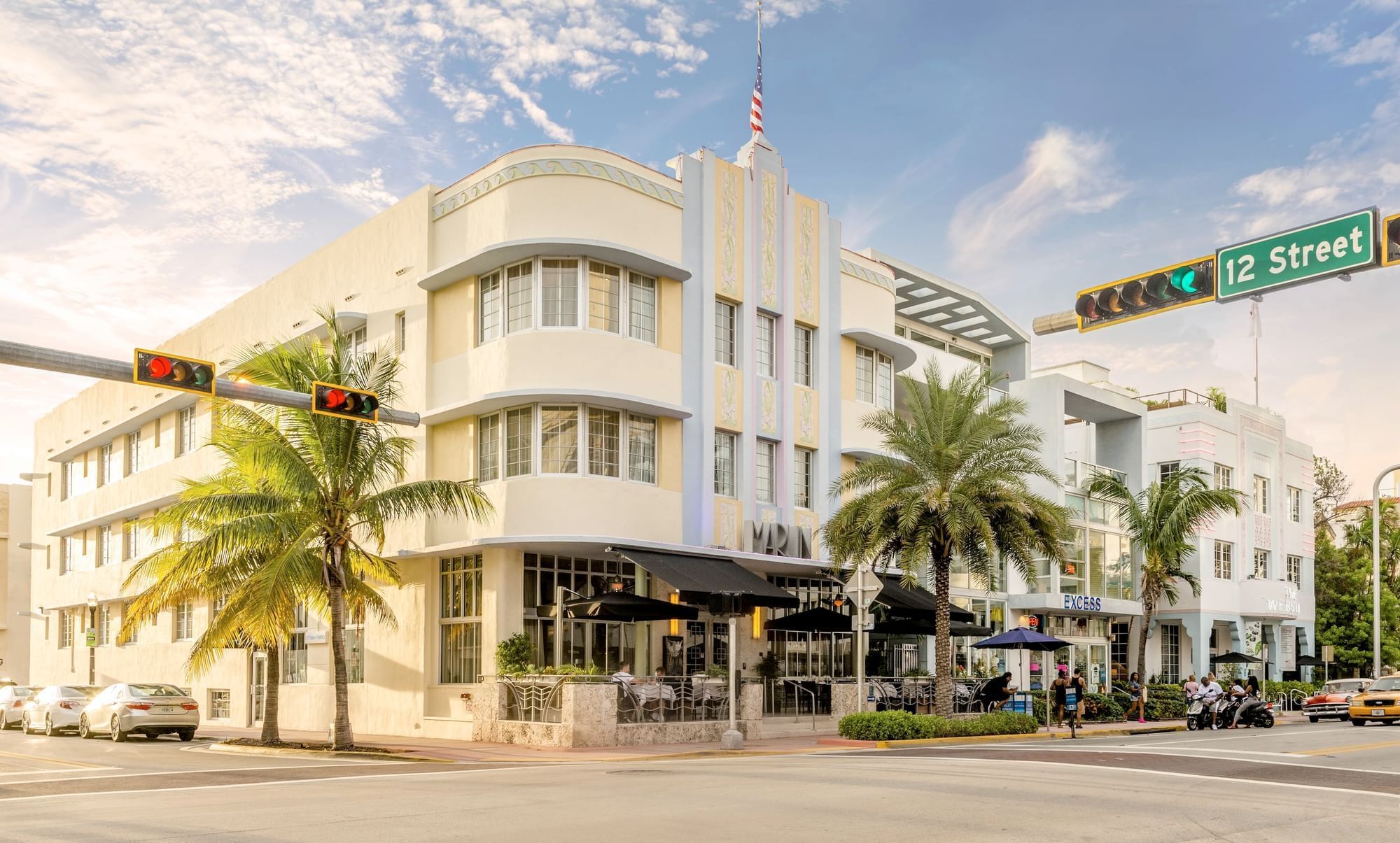 A white, multi-story building with palm trees and umbrellas on a street corner.